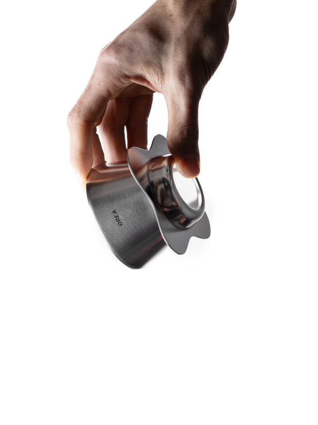 Hand holding an OREA 01 raw steel coffee dripper on a white background