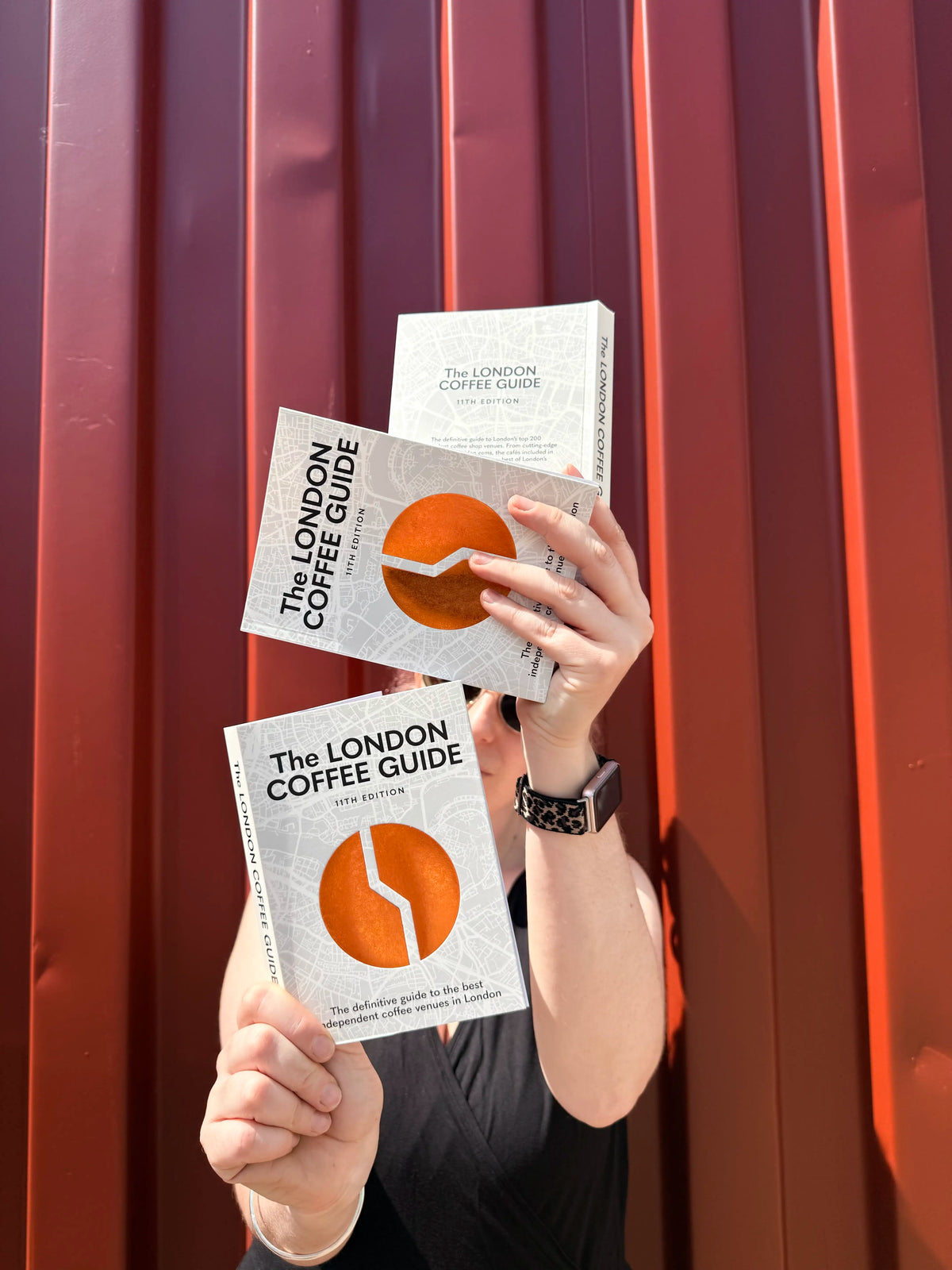 Person holding multiple copies of 'The London Coffee Guide' against a red background