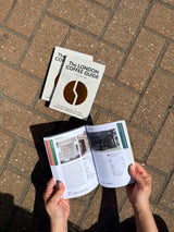 Person holding 'The London Coffee Guide' on a brick pavement