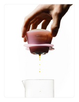 Hand holding a Creamy pink OREA 01 brewer with a clear container below on a white background