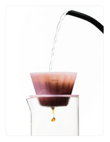 Creamy pink OREA 01 brewer being used to brew coffee into a glass.