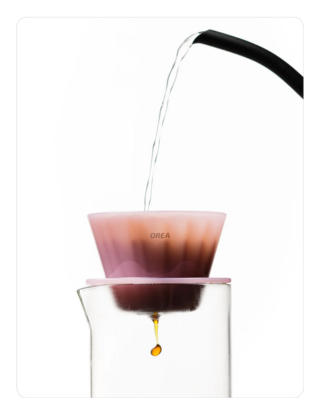 Creamy pink OREA 01 brewer being used to brew coffee into a glass.