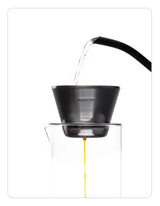 OREA 01 raw steel coffee dripper being used to brew coffee into a glass vessel on a white background